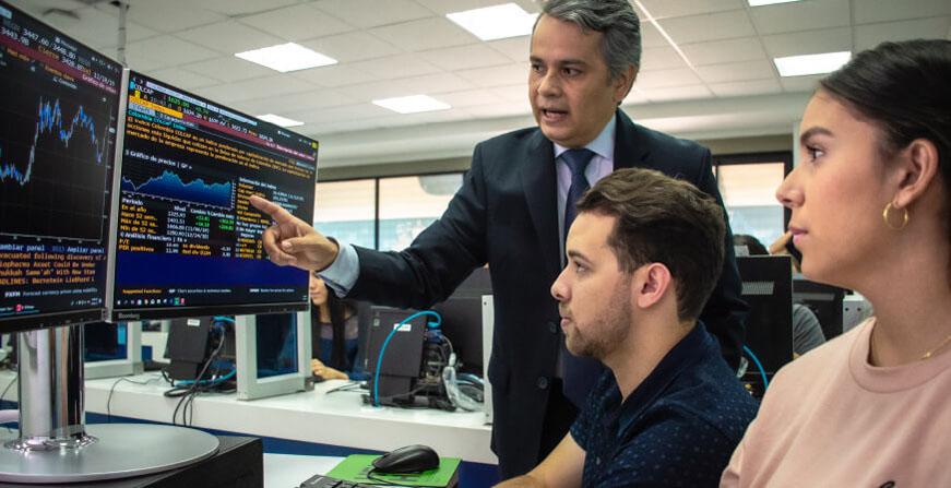 Estudiantes de Finanzas en Javeriana Cali Profesor y estudiantes de finanzas revisando cifras y comportamiento de la bolsa