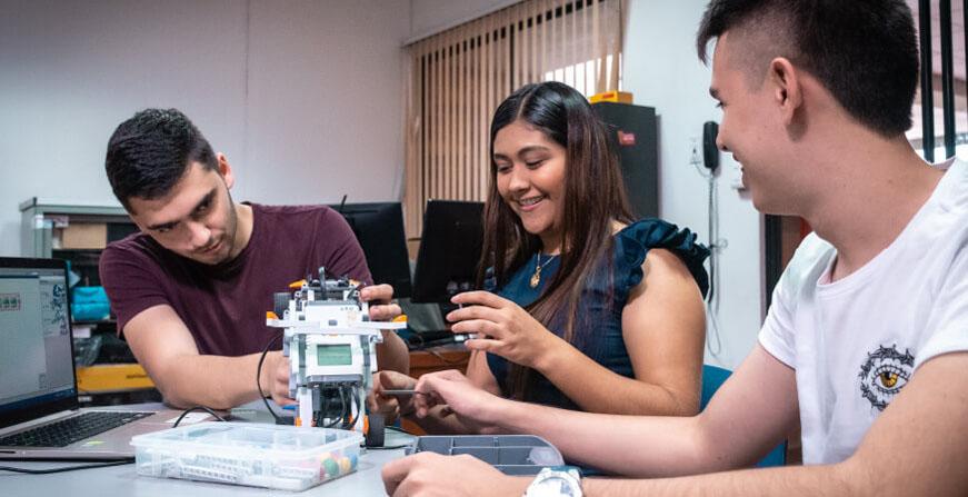 Estudiantes de Ingeniería de Sistemas y Computación Grupo de jóvenes revisando máquina y computador en un laboratorio de la universidad