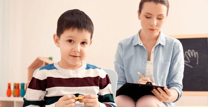 Especialización en Neuropsicología Infantil Niño jugando con ficha y mujer tomando nota del comportamiento